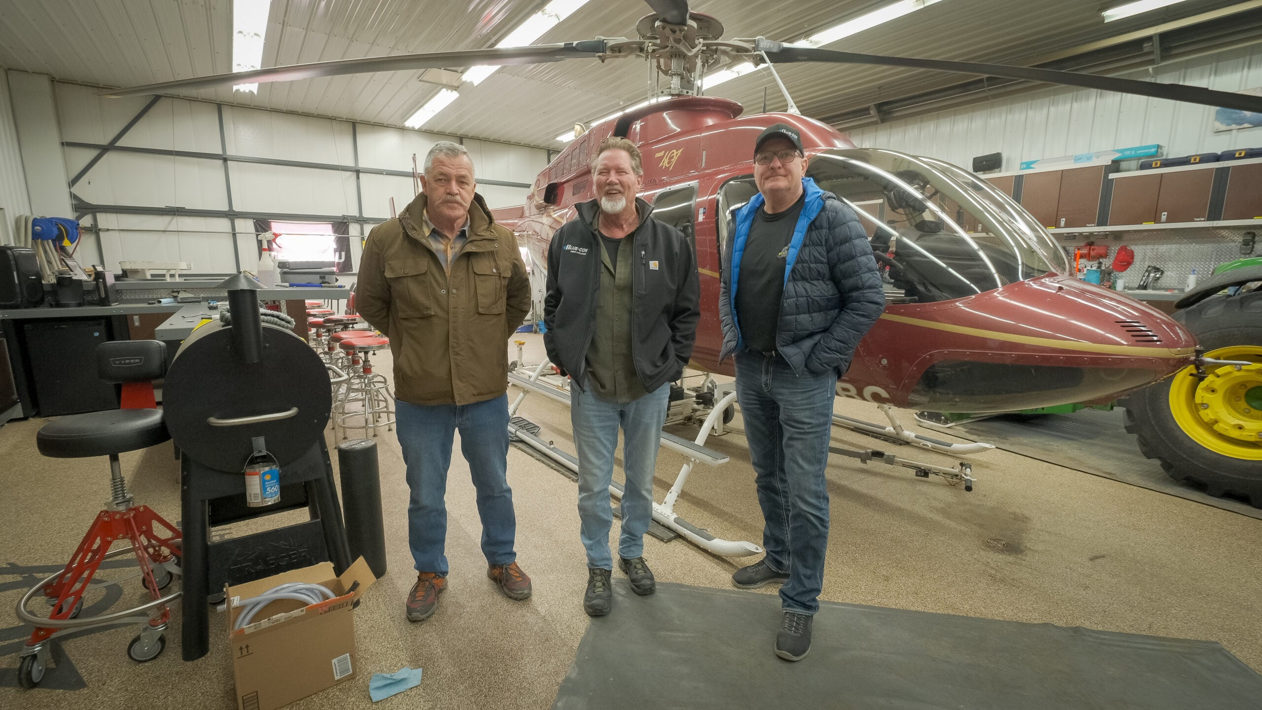 3 men standing next to a helicopter in a hanger space