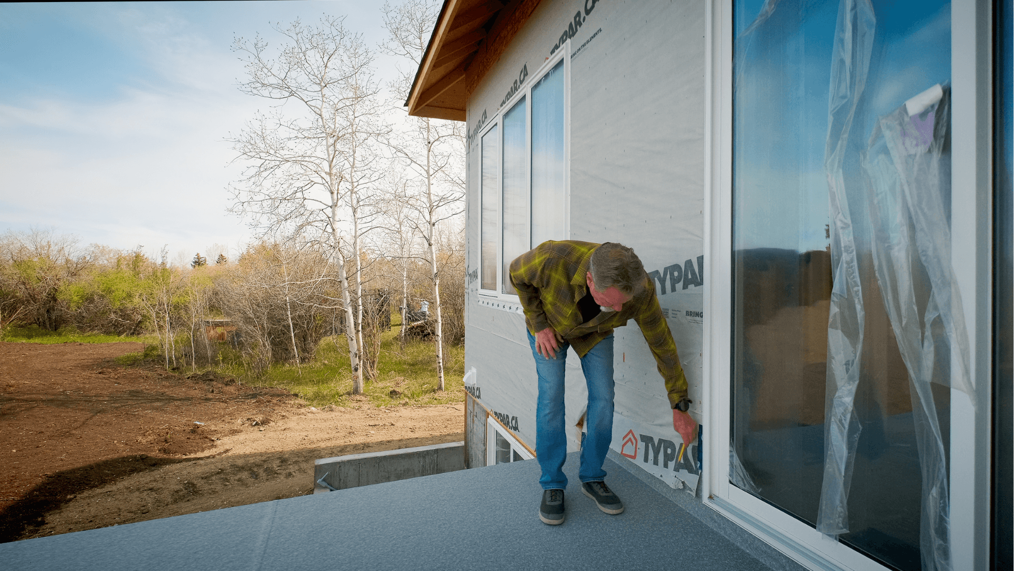 Builder bending down and inspecting the joint between a deck and the house