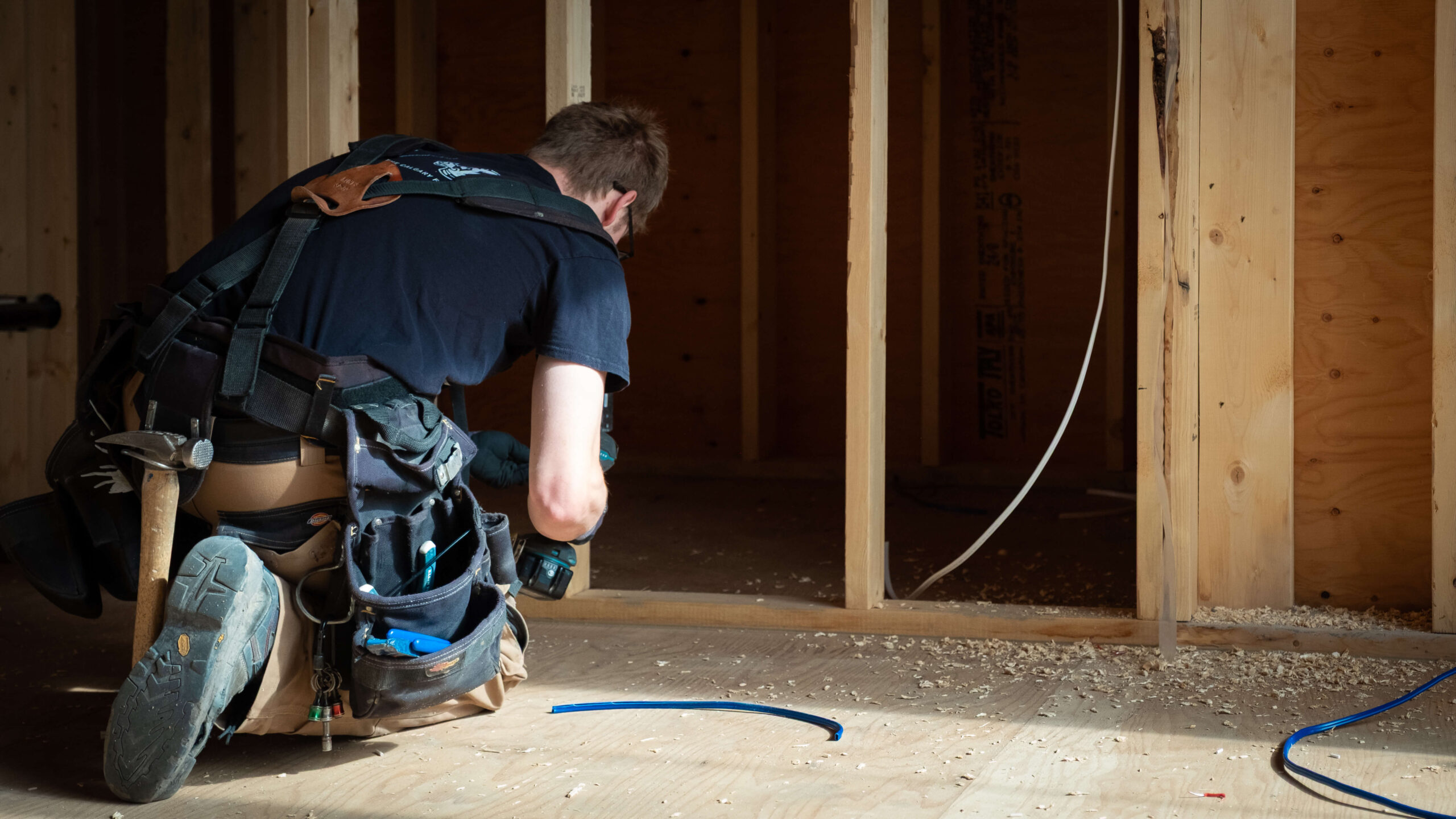 Electrician kneeling down , adding wiring to open framing in a new home construction