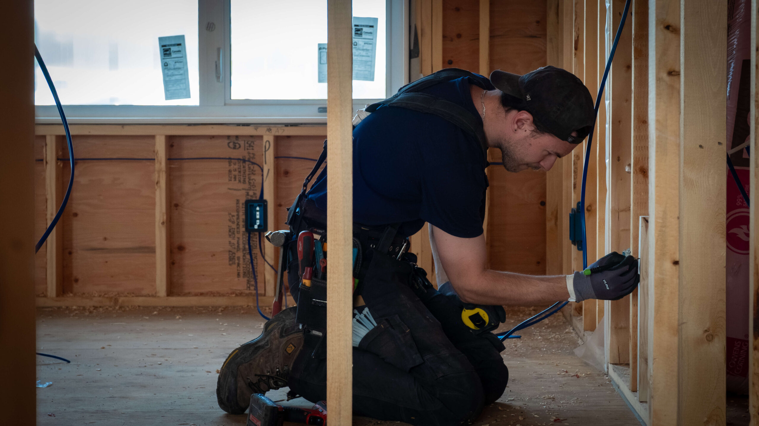 Electrician kneeling down , adding wiring to open framing in a new home construction