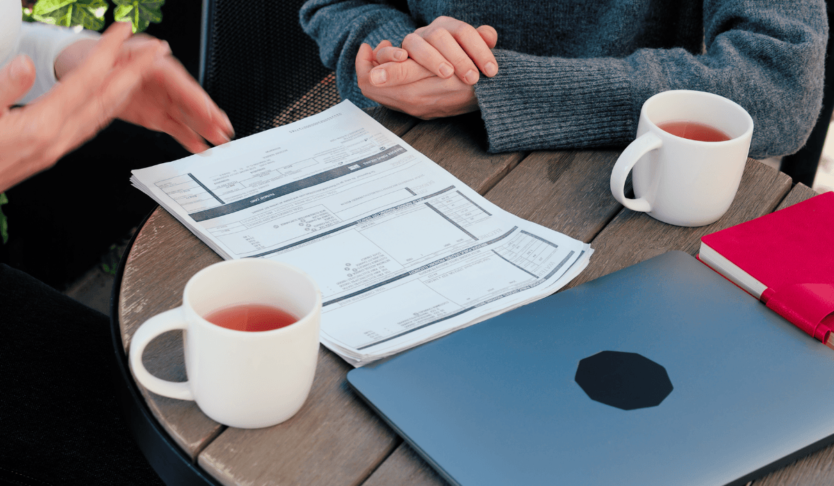 Two people sitting at a table, with hot drinks, discussing a document that is on the table